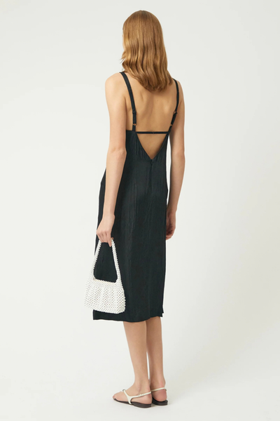 Full-length studio rear view of a model carrying the oat mini bag alongside a black slip dress and sandals.