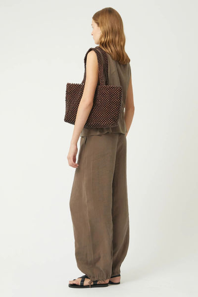 Studio side-profile view of a model carrying the dark chocolate lotus wood beaded tote bag under her arm.
