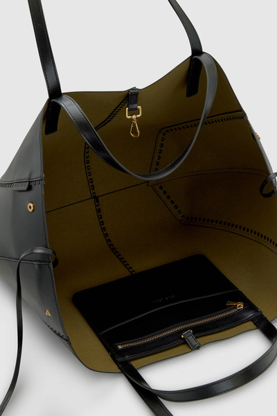 High-angle interior product detail shot of the open Brie Leon Reese Market Tote in black, showcasing the olive-green suede lining, gold dog-clip closure, and internal zippered drop pocket with debossed branding.