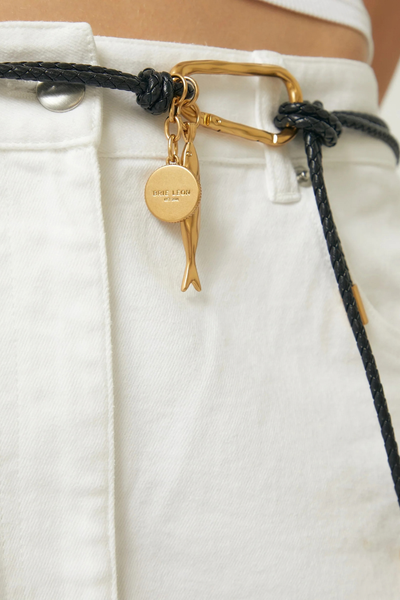 Close-up product view of the belt worn through white trousers, showcasing the knotted leather styling and gold hardware details.