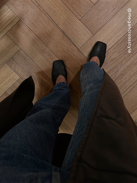 Point-of-view shot looking down at Senso Brynn black leather high-cut flats worn on herringbone wooden flooring, styled with blue jeans and a brown coat.