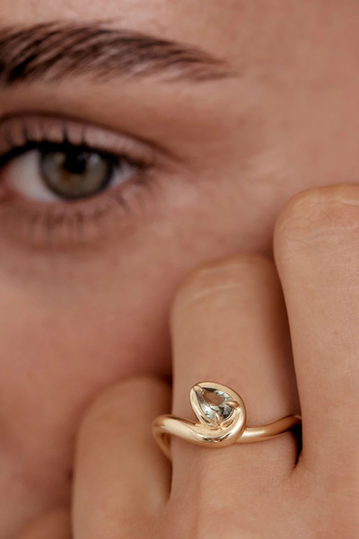 Close-up lifestyle shot of a model wearing the By Charlotte Embrace Growth Ring in 18k Gold Vermeil with green tourmaline, resting her hand near her face.