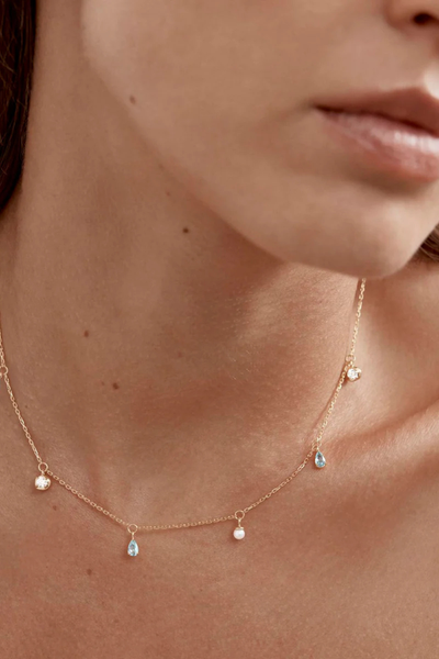 A portrait lifestyle image featuring the 18k gold plated choker on a model, highlighting its 16-inch length and showing the delicate drape of the ocean-inspired colorful gemstone and pearl charms against the skin.