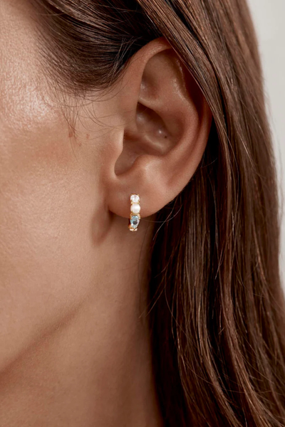 A macro lifestyle shot from a slight side angle of the gold gemstone hoop earring on a model's ear, highlighting how the ocean-inspired tones of the mint green nano gemstone and freshwater pearl catch the light during a soft-focus campaign shoot.