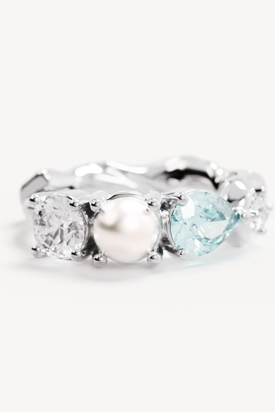 A macro close-up studio product shot highlighting the detailed frontline setting of a single sterling silver huggie hoop earring, focusing on the fine prongs holding a brilliant-cut round cubic zirconia crystal, a smooth round white freshwater pearl, and a teardrop-shaped light mint green tourmaline gemstone.