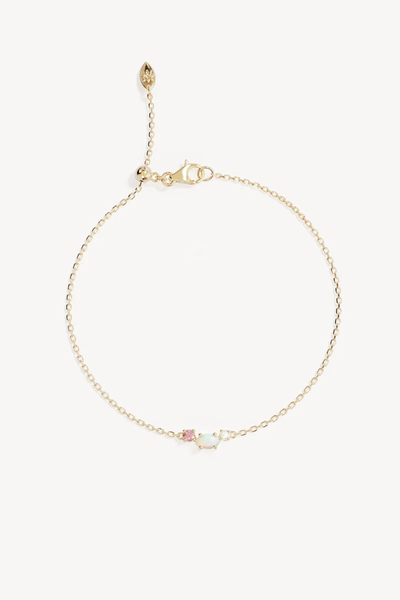 Studio product shot of the By Charlotte Cosmic Bloom Bracelet in 18k Gold Vermeil laid flat against a white background, featuring a delicate diamond-cut cable chain centered with a trio of a round pink cubic zirconia, oval lab-grown opal, and small freshwater pearl, complete with a silicone ball slider and lobster clasp.