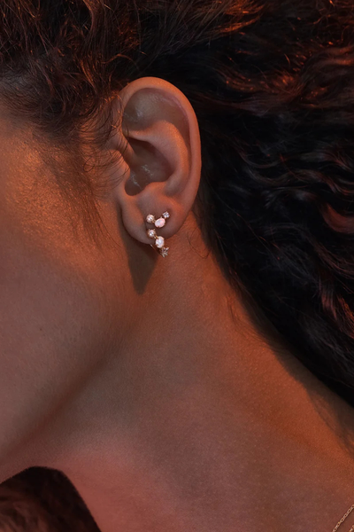 On-model detail view of the By Charlotte Cosmic Bloom Hoop in 18k Gold Vermeil styled in an ear stack under warm ambient lighting.