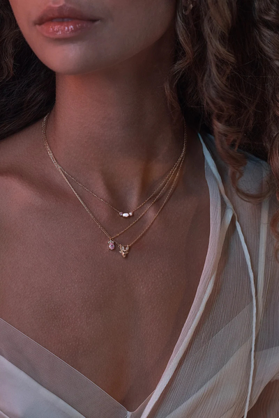 On-model lifestyle detail shot showing the By Charlotte Cosmic Bloom Necklace in 18k Gold Vermeil layered with other gold pendant necklaces in warm ambient light.