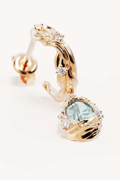 A close-up shot focusing on a single gold hoop earring from an elevated angle, detailing the high-polish finish of the twisted metal design, the small prong-set cubic zirconias embedded into the hoop, and the fluid gold casing surrounding the vibrant mint green teardrop gemstone.