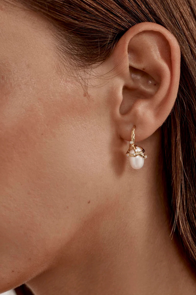 A lifestyle image showing a close-up profile view of a model wearing the gold vermeil Dive Into Serenity Pearl Earring, illustrating how the statement baroque pearl drops and reflects natural light, complementing a casual updo hairstyle.