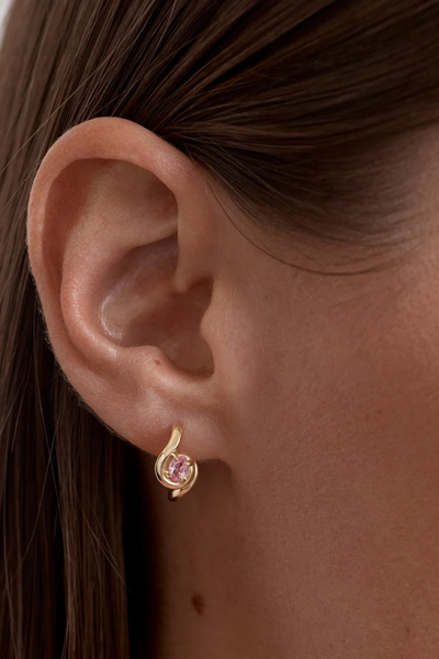On-model detail shot of the By Charlotte Embrace Love Hoop in 18k Gold Vermeil worn in the earlobe, demonstrating the fit and placement of the pink gemstone huggie hoop.