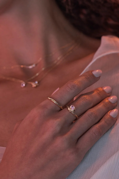 On-model lifestyle detail shot of the By Charlotte Embrace Love Ring in 18k Gold Vermeil stacked with a gold band, set against warm atmospheric lighting.