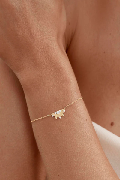 A minimal lifestyle campaign image of the 18k gold vermeil Lotus Rain fine chain bracelet being worn on a model's wrist, illustrating how the textured semi-circle cubic zirconia pendant drapes delicately against the skin.