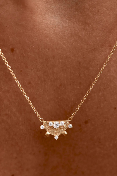 A wider lifestyle portrait showing the gold lotus-inspired talisman necklace being worn by a model, capturing the full drape of the signature fine chain to showcase its adjustable 18-inch length and delicate silhouette.