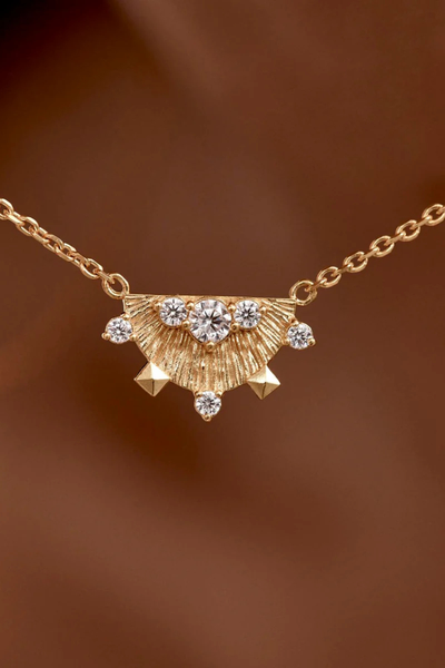 A macro, angled close-up studio shot of the 18k Gold Vermeil Lotus Rain pendant resting on a reflective white surface, detailing the textured metal finish, the lobster clasp chain attachment, and the precision prong settings of the clear cubic zirconia stones.