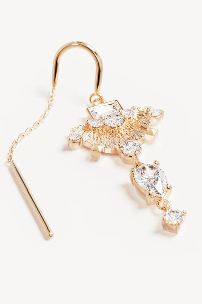 A flat lay studio shot of a single 18k gold vermeil thread earring resting on a white surface, detailing the sleek post, fine cable chain, and the intricate gemstone arrangement featuring contrasting claw and bezel settings on the fan pendant and crystal drops.