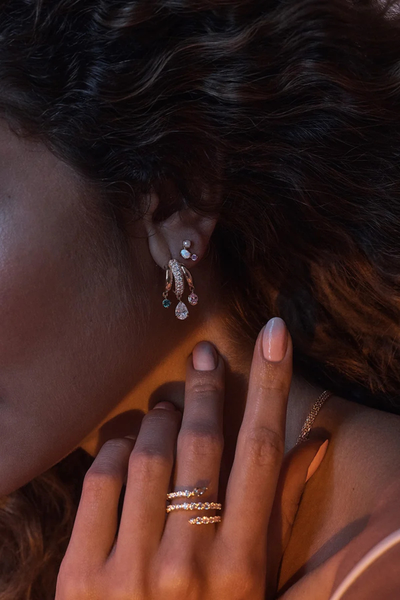 On-model lifestyle shot showing the By Charlotte Vibrant Soul Illusion Hoop styled in an ear curation with matching gold rings in warm ambient lighting.