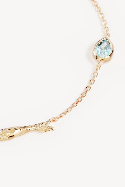 A macro close-up studio shot detailing the craftsmanship of the fine gold chain, highlighting the multi-dimensional textures of the small sculpted gold anchovy charm and the light reflection on the faceted, bezel-set teardrop mint green tourmaline nano gemstone pendant.