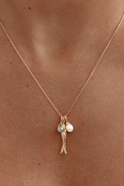 A macro close-up studio shot of the three gold charm pendants cluster suspended from the fine chain over a seamless white background, capturing the high-shine finish of the 2cm anchovy pendant, the light blue-green shimmer of the faceted teardrop tourmaline charm, and the smooth luster of the natural freshwater pearl.