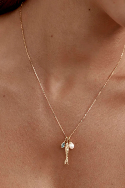 A slightly wider campaign portrait showing the gold Wishing Necklace on a model, highlighting the overall scale and drape of the signature fine chain, illustrating its adjustable 19-inch length and playful, ocean-inspired design.