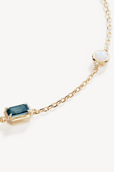 Macro close-up shot of the By Charlotte You Are Infinite Bracelet in 18k Gold Plated, detailing the fine link gold chain, bezel-set lab-grown opal, and emerald-cut green tourmaline gemstone.