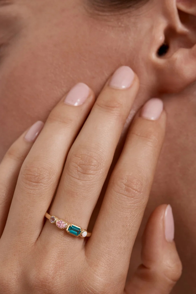 Close-up lifestyle shot of a model wearing the By Charlotte You Are Infinite Ring in 18k Gold Vermeil with multi-colored gemstones, resting her hand near her face.