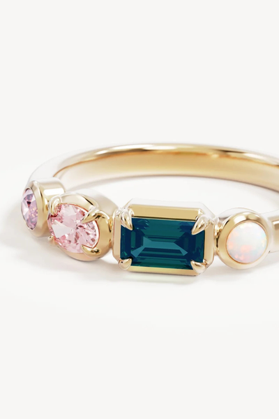 Extreme close-up product shot of the By Charlotte You Are Infinite Ring in 18k Gold Vermeil, highlighting the bezel-set multi-gemstone arrangement of pink cubic zirconia, nano tourmaline paraiba, and lab-grown opal.
