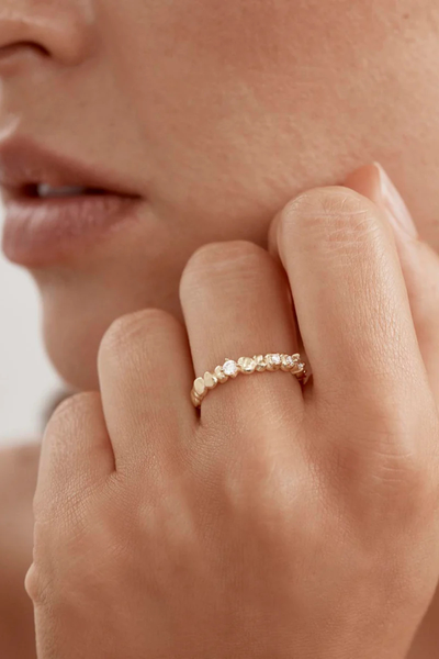 A lifestyle campaign image featuring a close-up of the textured gold Endless Summer Ring being worn on a model's hand, illustrating its delicate scale as a fine band and demonstrating how it sits elegantly against the skin for everyday styling or stacking.