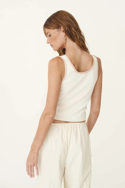 Rear view of a blonde model wearing the ROWIE Blake Contrast Knit Tank in Oat Milk with cream pants, displaying the low scoop back and subtle contrast trim along the neckline and armholes.