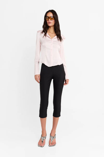 Full-length front view of a model standing against a white background, wearing the pink fitted shirt, tinted sunglasses, black capris, and zebra-print heels.