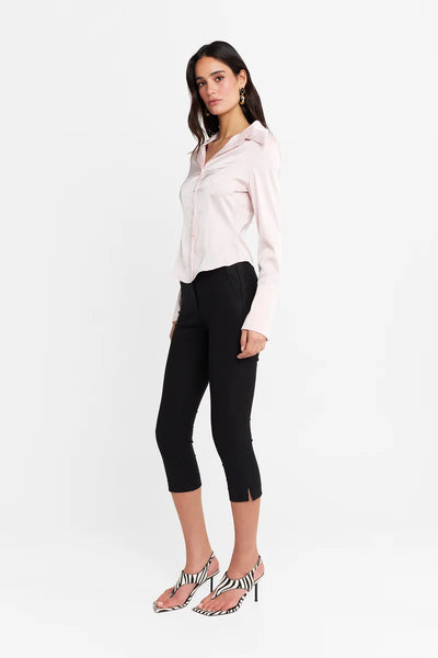 Three-quarter side profile view of a model wearing the pink long-sleeve shirt and black capri pants, showing the architectural angled hemline and side silhouette.