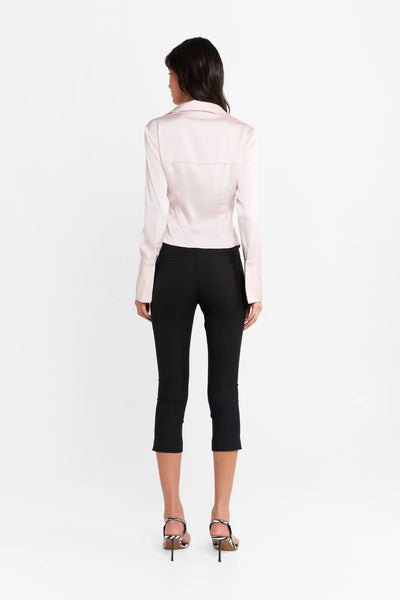 Full-length back view of a model wearing the black stretch-suiting capri pants paired with a light pink satin long-sleeve blouse and zebra-print heeled sandals.