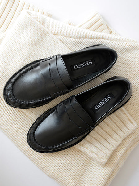 Flat lay shot of Senso Cooper III ebony leather loafers with classic penny straps resting on a folded cream ribbed knit sweater.