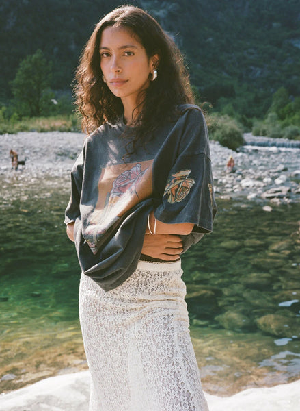 Outdoor lifestyle shot of a model wearing the oversized Kinga Csilla Desert Rose OG Tee in stonewashed black styled with a sheer white lace skirt.