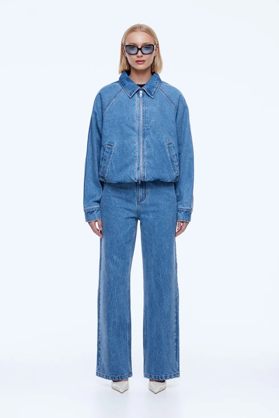 Full-length studio shot of a model wearing the oversized ENA PELLY Billy Denim Bomber in Light Indigo paired with matching wide-leg jeans and pointed heels.