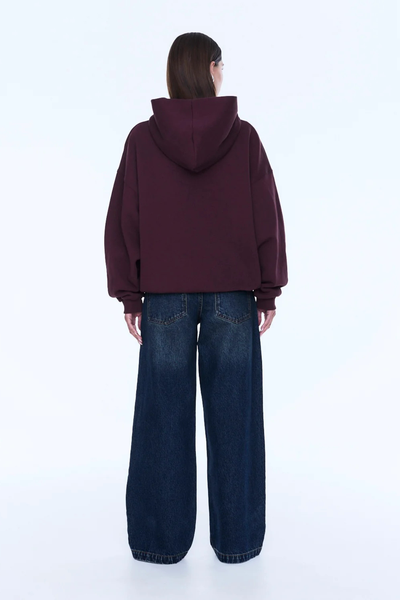 A full-length profile shot capturing the back view of the model wearing the cherry red graphic hoodie. This angle showcases the deep slouchy silhouette of the self-lined hood, the comfortable drop-shoulder seam construction, and the generous volume of the long sleeves.