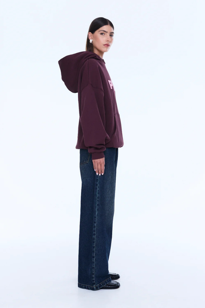 A cropped three-quarter front portrait focusing on the upper body, illustrating the uniform deep cherry red tone of the cotton-blend fleece, the loose fit of the long sleeves ending in ribbed cuffs, and the front kangaroo pouch pocket.