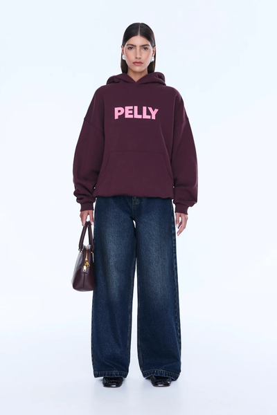 A full-length front view of the model standing highlighting the structural hang of the rib cuffs and hem band on the oversized cotton-rich fleece garment.