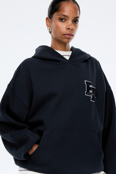 A close-up crop focusing on the face and upper torso of the model from an angle. The shot emphasizes the rich, faded depth of the washed midnight tone, the structural fold of the fleece hood, the detailed embroidery texture of the left-chest logo, and the model's metallic gold earrings.