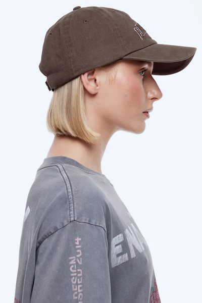 Side profile studio shot of a blonde model wearing the ENA PELLY Collegiate Cap in Washed Mocha, showing the six-panel dad cap design and curved brim paired with a washed grey graphic tee.