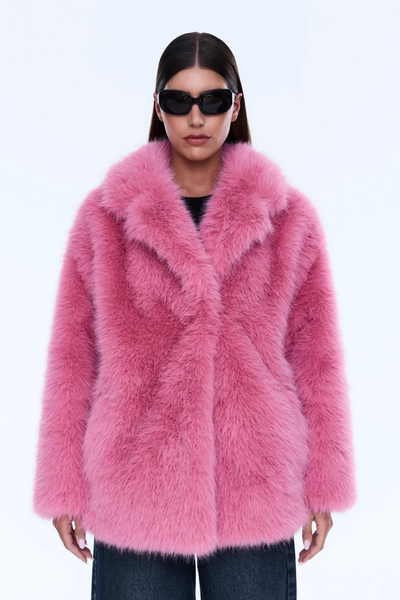 A full-length, straight-on front view of the model standing with arms at their sides, highlighting the uniform bright pink coloration, the notched lapel collar, and the boxy, oversized fit of the outerwear piece paired with dark wide-leg jeans.
