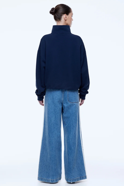 Rear full-length view of a model in studio lighting showing the relaxed back fit and dropped shoulders of the navy ENA PELLY Kenzie 1/4 Zip Jumper styled with wide-leg denim jeans.