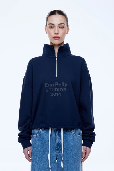 Front half-body studio shot of a model wearing the dark navy ENA PELLY Kenzie 1/4 Zip Jumper with the silver zipper pulled up, high neck collar, and ribbed cuffs.