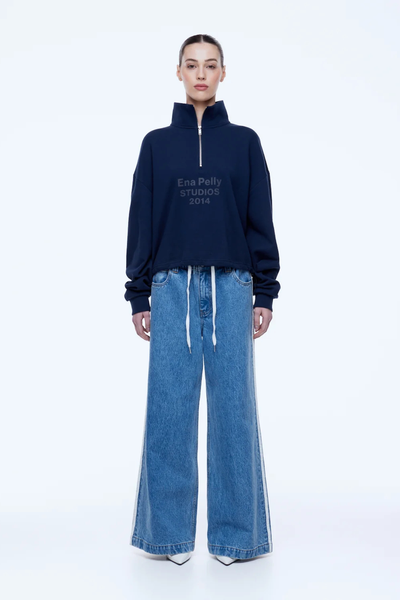 Full-length front studio portrait of a model standing in the oversized navy ENA PELLY Kenzie 1/4 Zip Jumper, styled with wide-leg light blue jeans with white drawstring details.