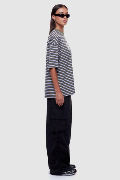 Studio side profile view of a model wearing an oversized striped graphic t-shirt with drop shoulders paired with wide-leg black cargo trousers.