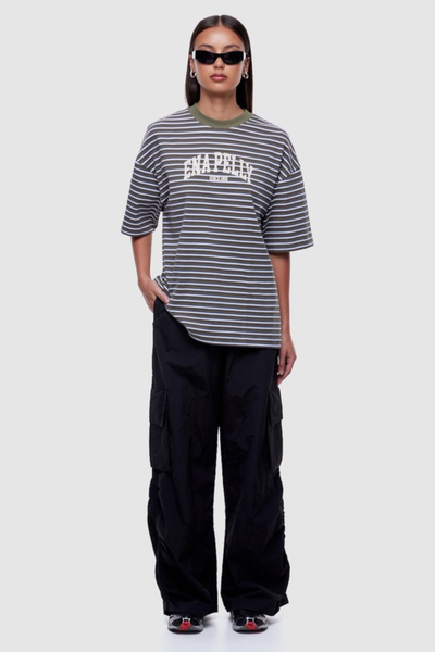 Full-length studio front shot of a model wearing an oversized green horizontal striped crew-neck tee paired with loose-fitting black trousers.