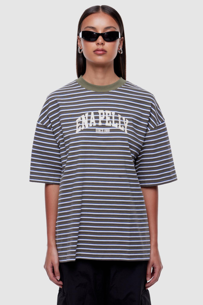 Studio front view of a model wearing dark sunglasses and an oversized green, grey, and white striped short-sleeve t-shirt with a olive green ribbed crew neck and collegiate "Ena Pelly" arch graphic print across the chest.
