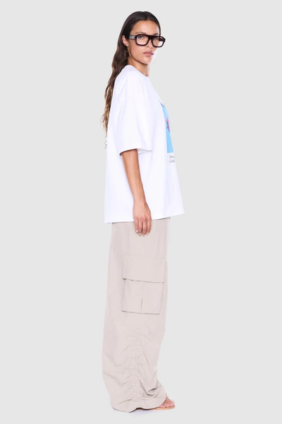 Studio side profile view of a model wearing an oversized white short-sleeve graphic tee paired with wide-leg beige cargo pants.