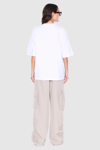 Studio rear view of a model showing the back cut, crew neckline, and drop shoulders of an oversized white t-shirt paired with beige pants.
