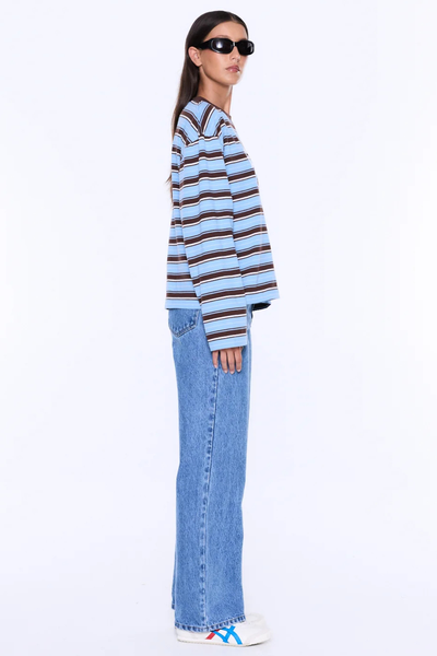Side profile studio portrait of a model wearing the blue and brown striped ENA PELLY Maria Boxy Long Sleeve Tee paired with relaxed blue jeans and sneakers.